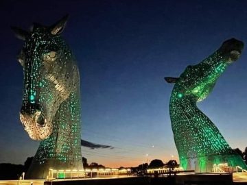 The Kelpies, Scotland, lit up in green against the night sky.