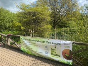 Leeds City Council banner Tick awareness banner attached to railings on a bridge with trees behind it