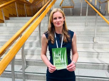Morven-May MacCallum holding Be Tick Aware postcard in front of the steps at Holyrood.