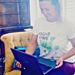 Natalie Hay, a parent carer, working on her laptop wearing a Fight Lyme T-shirt.